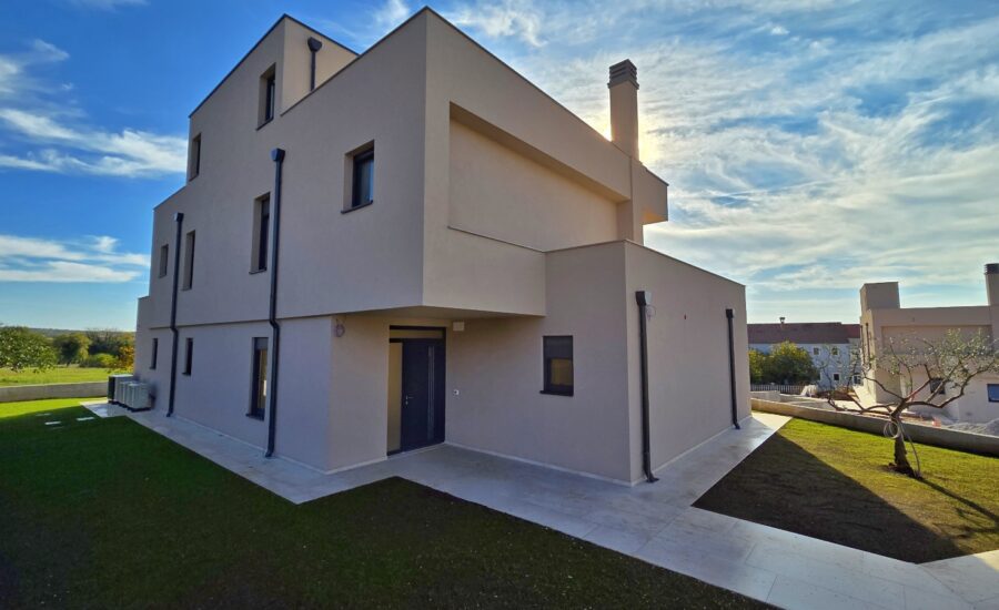 Contemporary home with angular architectural design, covered entryway, drainage pipes, and landscaped yard with young tree.