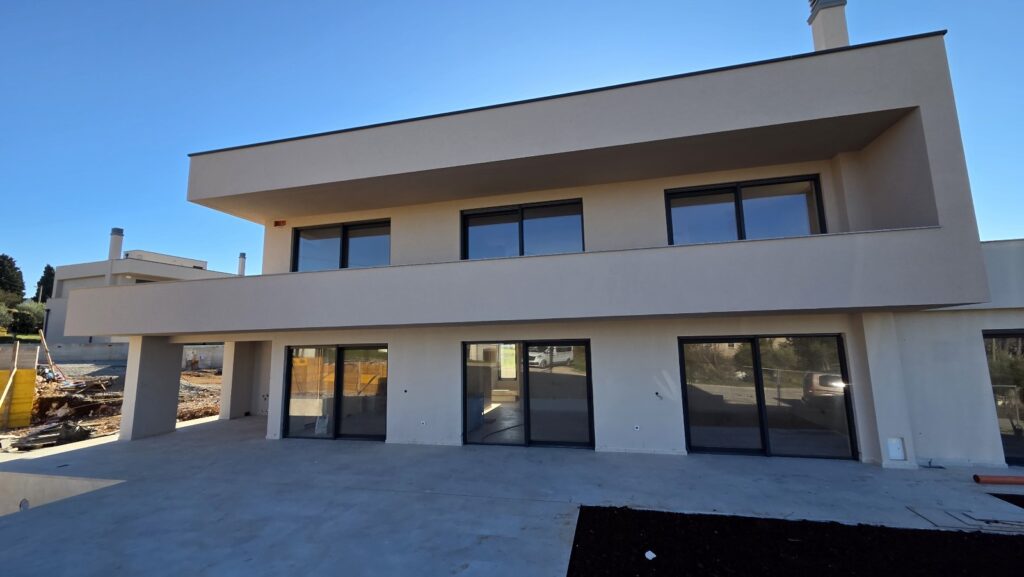 Newly built modern two-story home featuring a spacious terrace, floor-to-ceiling windows, and a tiled pool in the foreground.