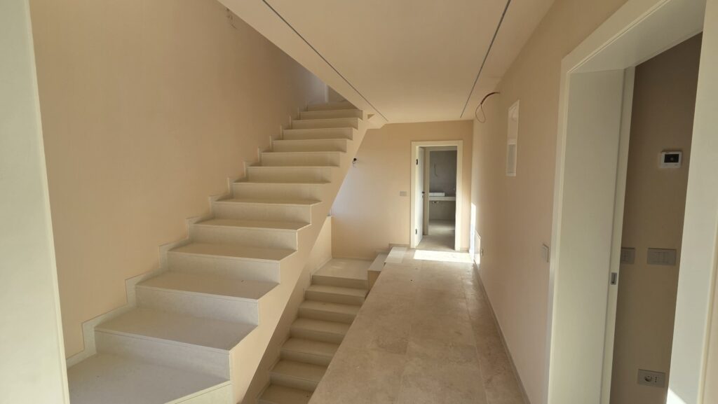 “Bright open-concept living space with large floor tiles, full-height windows, and staircase to the upper floor.”