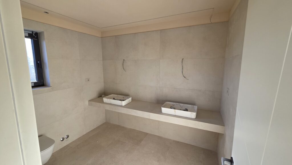 Compact modern bathroom with vessel sink on a floating countertop, wall-mounted toilet, and large beige tiles