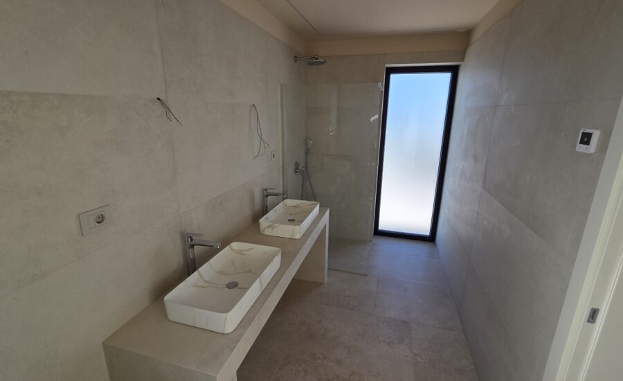 Contemporary bathroom featuring a wall-mounted toilet, rectangular vessel sink, and light stone tiles.