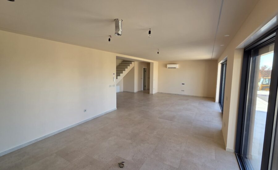 Open modern interior featuring light stone-look tiles, large windows for natural light, and a staircase connecting to the upper level.