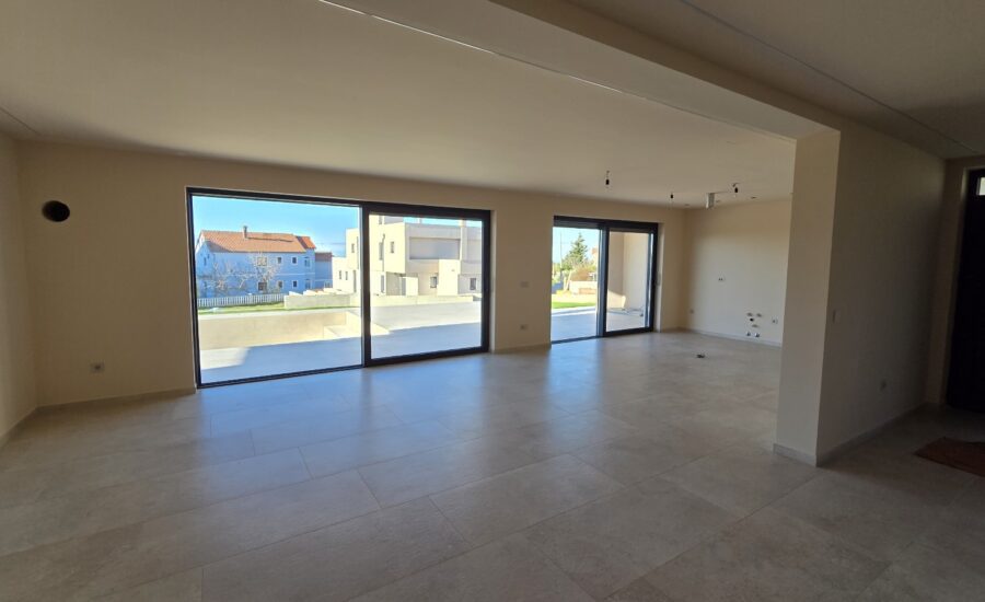 Open modern interior featuring light stone-look tiles, large windows for natural light, and a staircase connecting to the upper level.