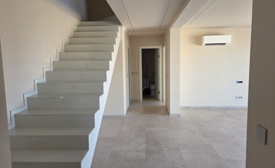 Open modern interior featuring light stone-look tiles, large windows for natural light, and a staircase connecting to the upper level.